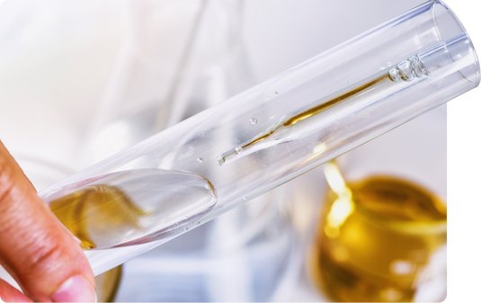 Hand holding test tube and dropper with amber liquid.